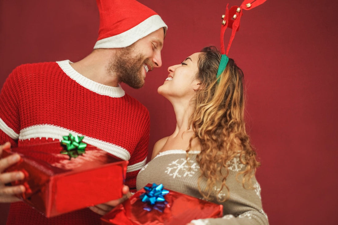 A smiling couple exchanging wrapped Christmas gifts in festive sweaters and Santa hats — perfect image for holiday gift ideas, Christmas sales, and seasonal product collections.