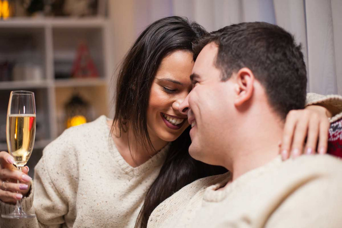 Romantic couple cuddling at home, smiling and sharing an intimate moment while holding a glass of champagne.