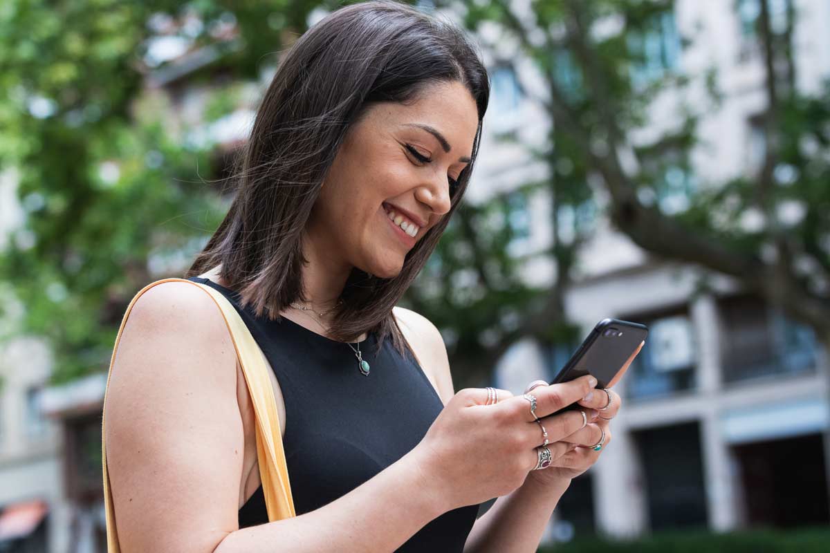 a young woman smiling while looking at her phone on the street