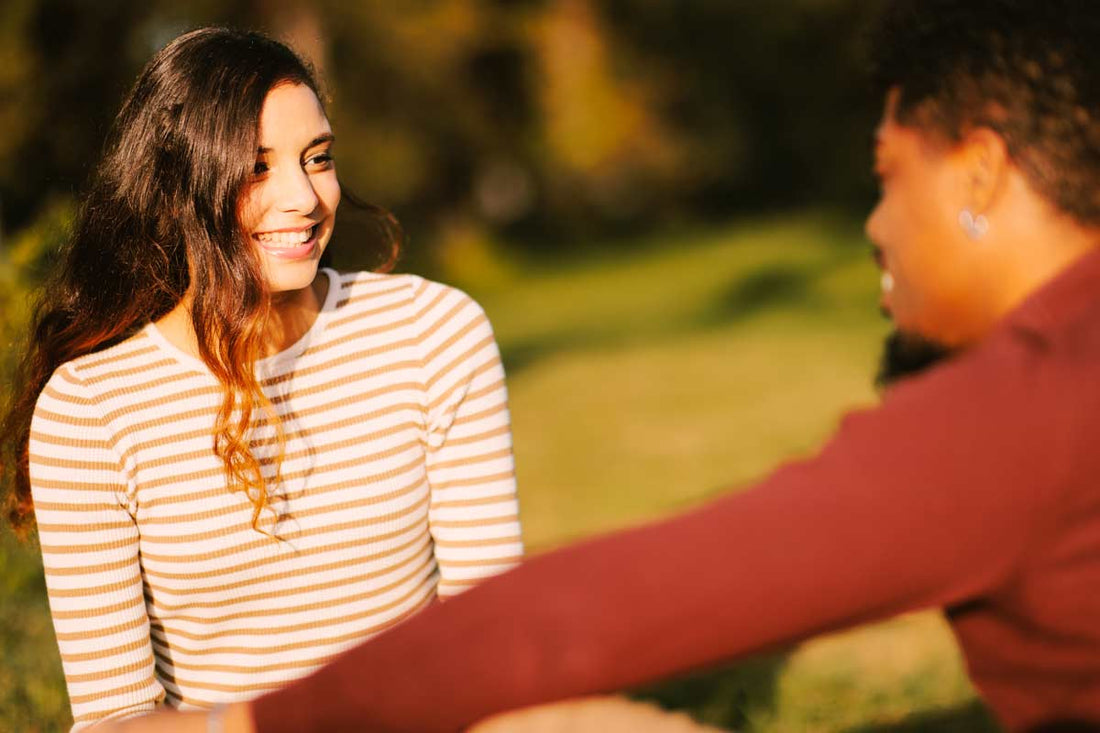 one young couple sitting in a park staring at each other in flirtatious way   